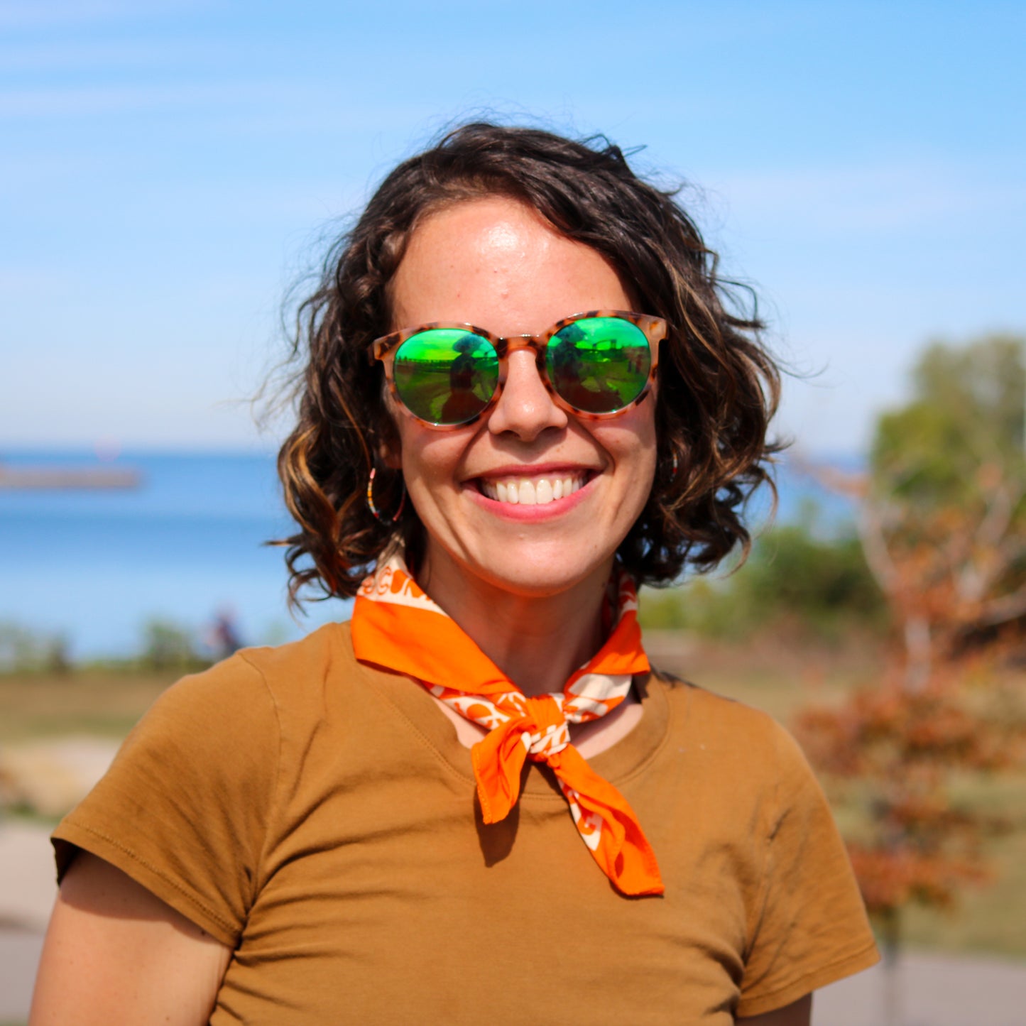 Person wearing sunglasses and an orange scarf with a blurred natural background