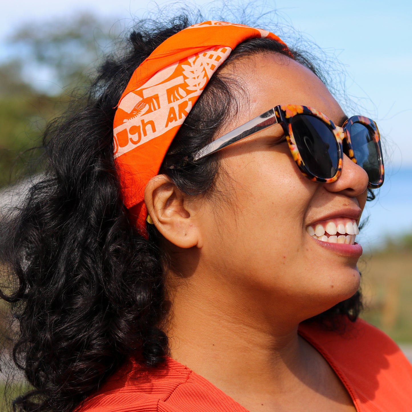 Woman wearing an orange headband and sunglasses with a blurred natural background