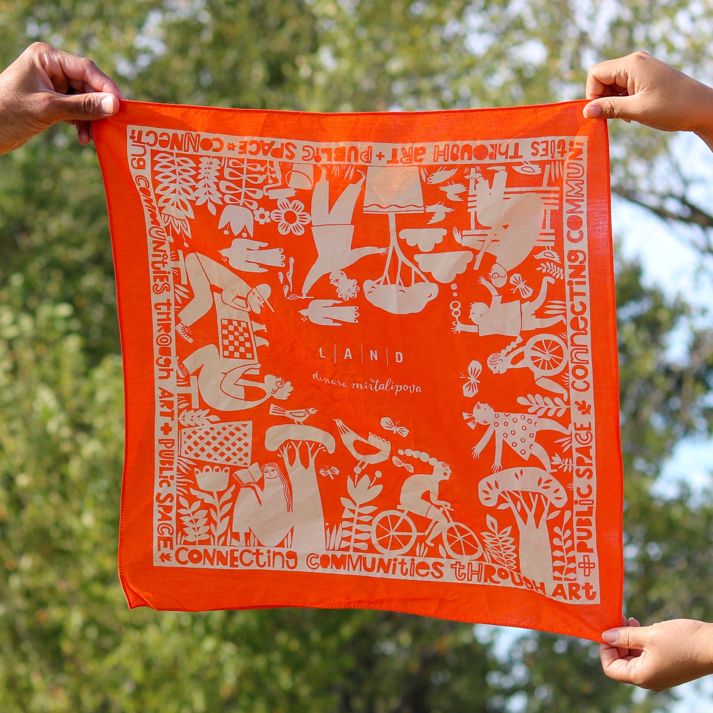 Orange bandana with white patterns and text held by hands against a blurred natural background