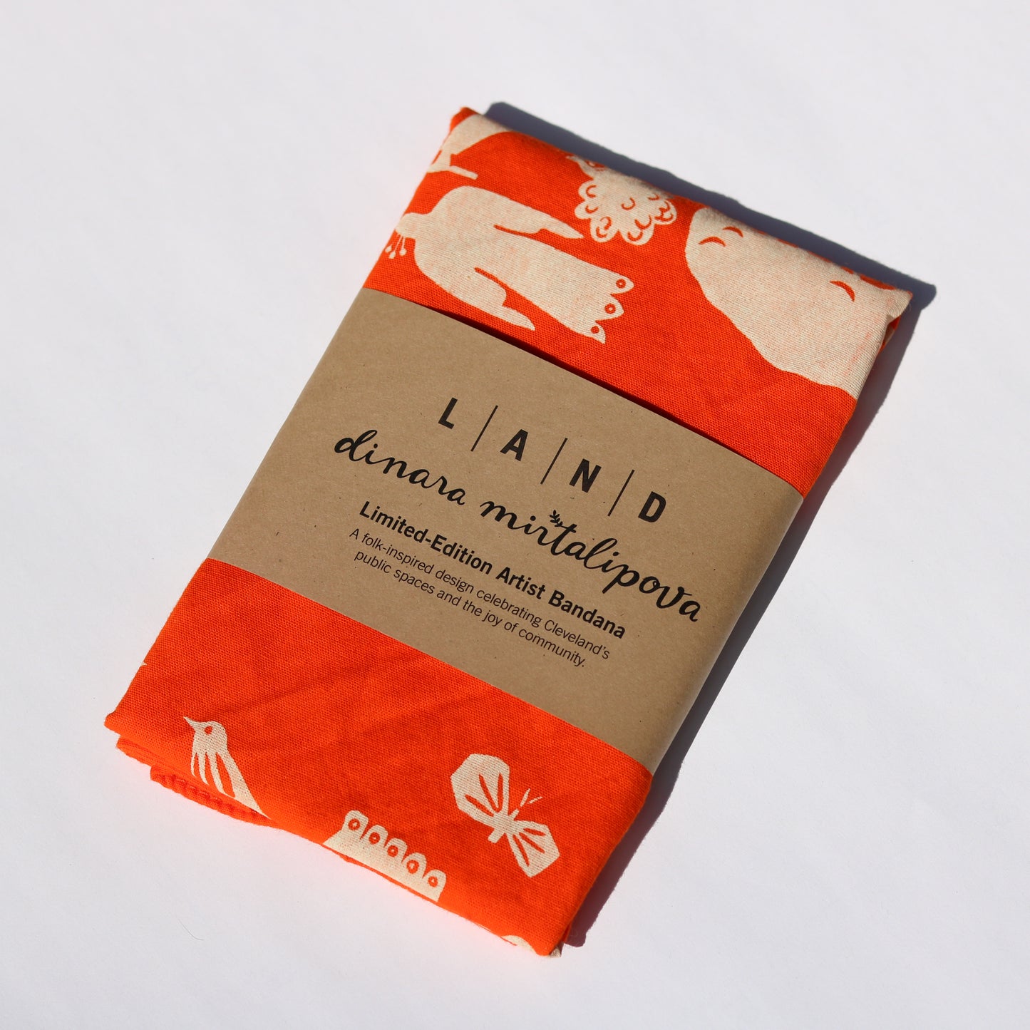 Orange bandana with white designs on a cardboard backing, featuring 'LAND dinara mirtalipova' branding.